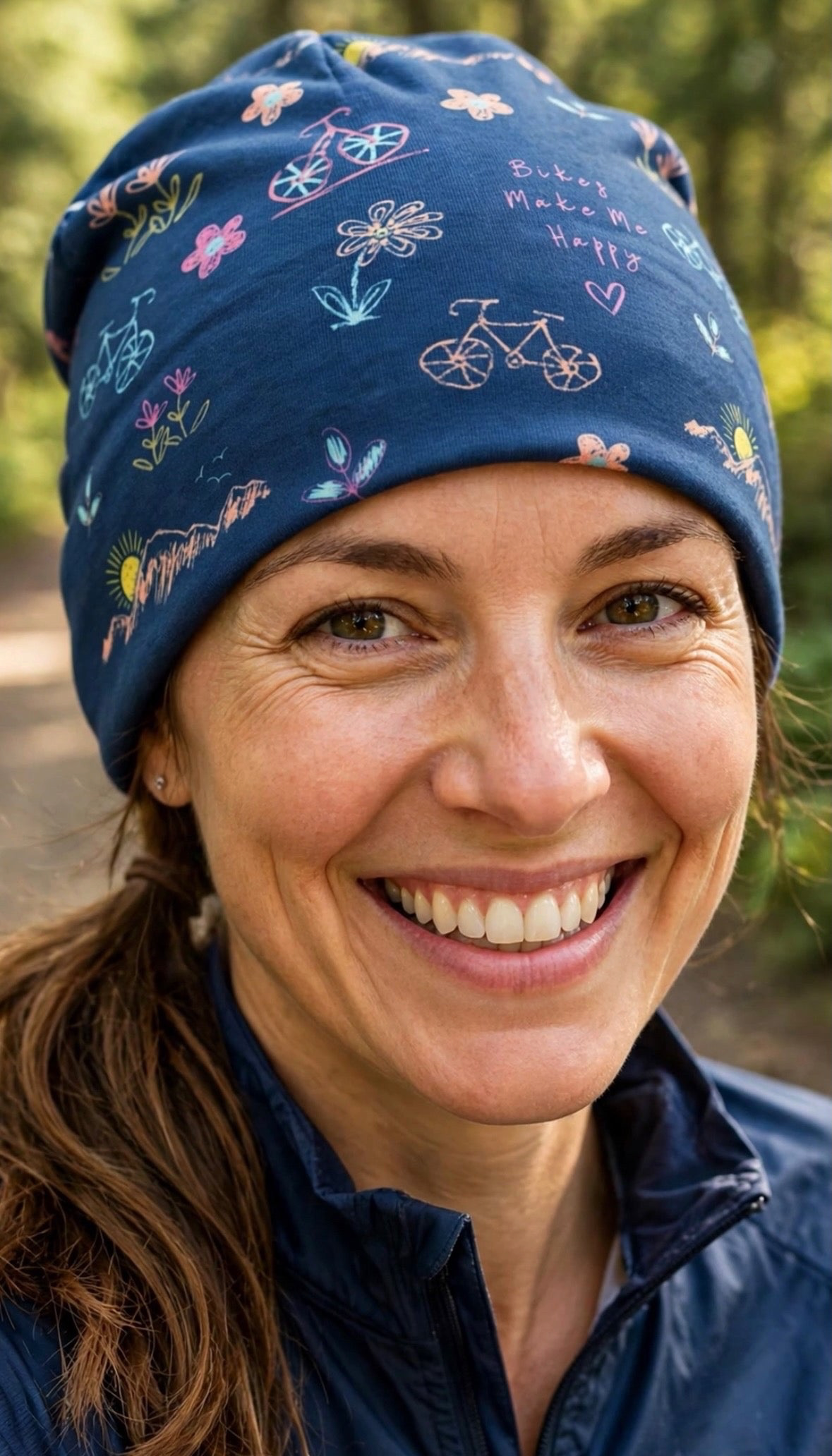 Bikes Make Me Happy Pedals and Petals lightweight blue beanie with bicycle and flower print worn by a smiling woman