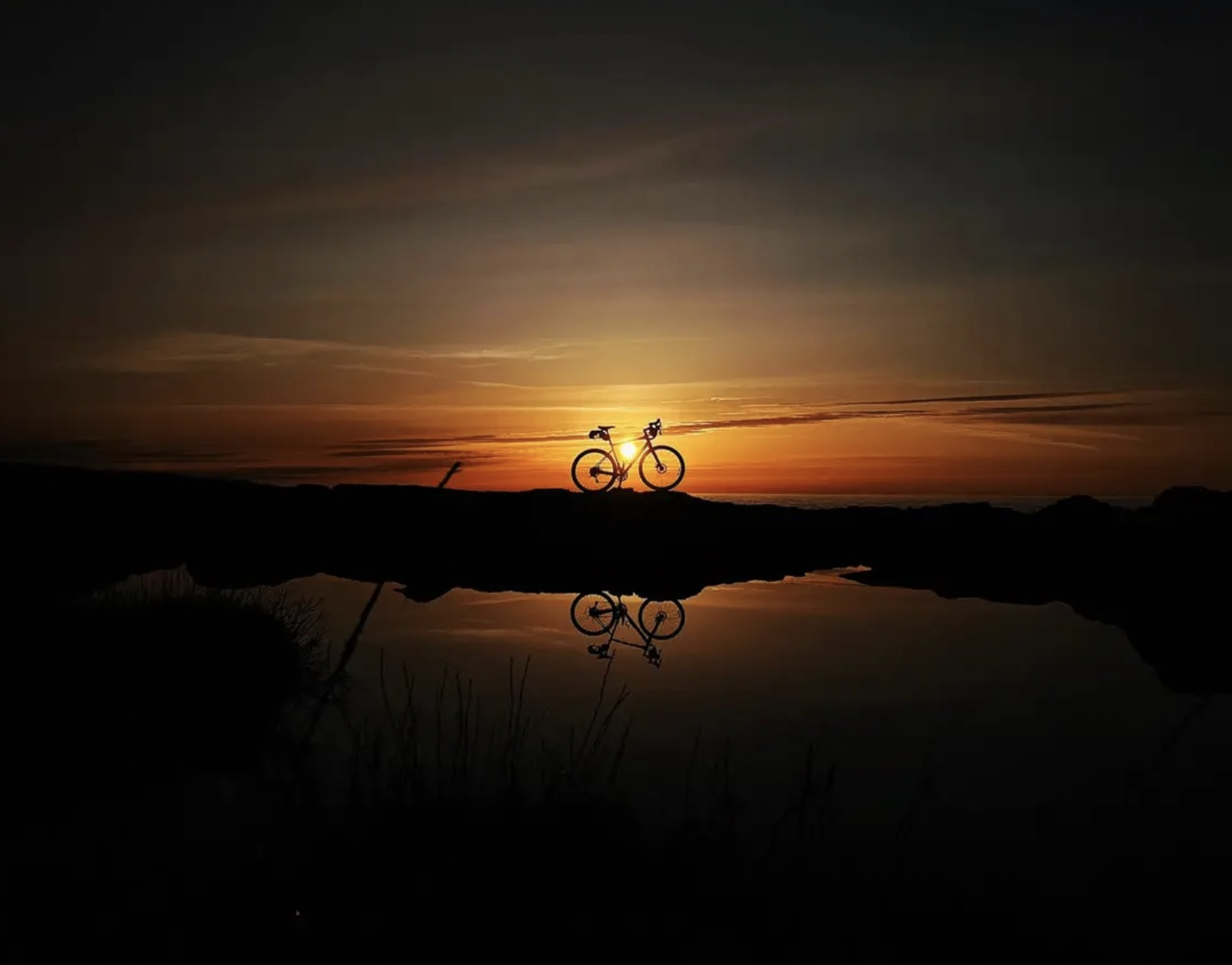 Two cyclists riding on a dirt trail with stunning mountain views and clear skies.